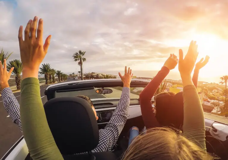 Happy friends having fun in convertible car at sunset in vacation - Young people making party and dancing in a cabrio auto during their road trip - Friendship, travel, youth lifestyle concept